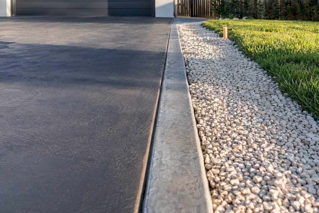 Concrete driveway edging beside gravel and lawn